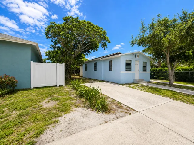 Light blue cottage with white trim, mature shade tree, and walkway to the front door.