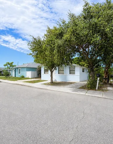 Light blue cottage with white trim, mature shade tree, and walkway to the front door.