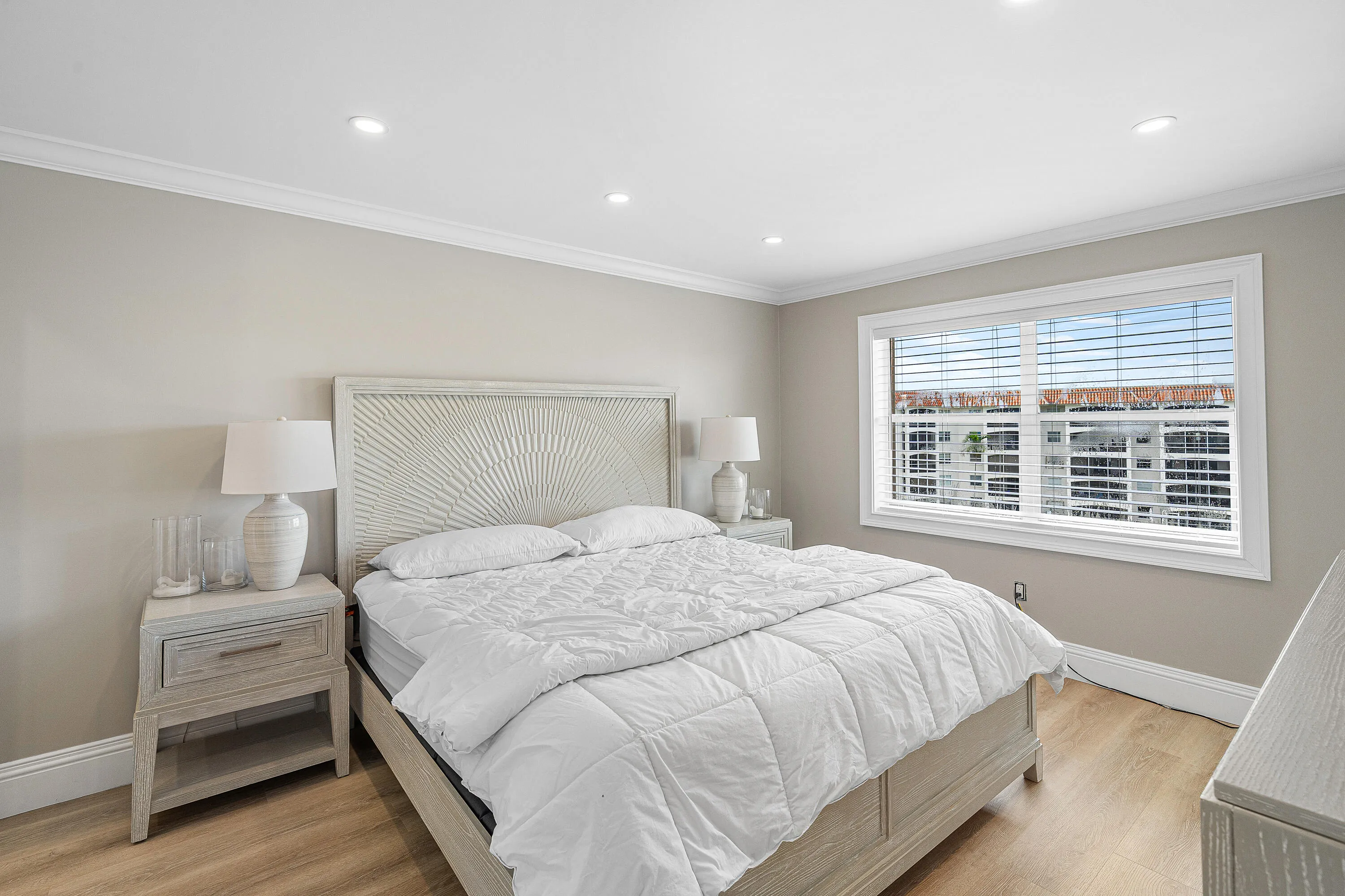 Serene primary bedroom showcasing a geometric-patterned upholstered headboard, wood-finish flooring, and recessed ceiling lighting