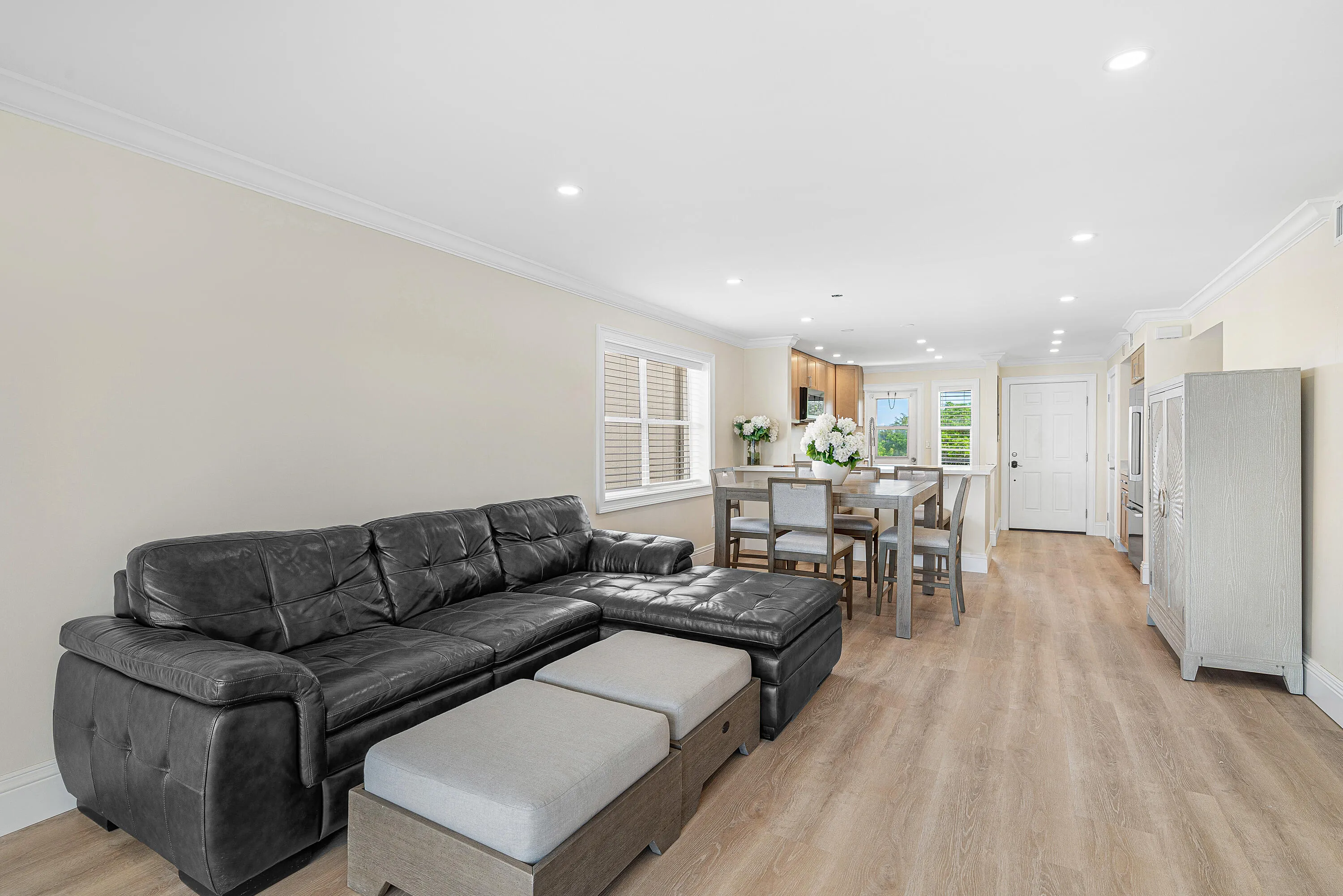 Open-concept living area with light wood-finish flooring, recessed lighting, crown molding, and a dining area
