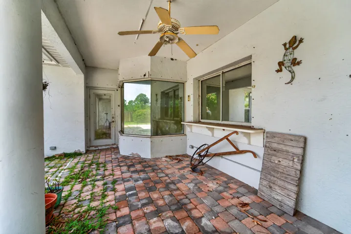 Brick paver patio with a white textured wall finish, featuring a ceiling fan and an exterior door