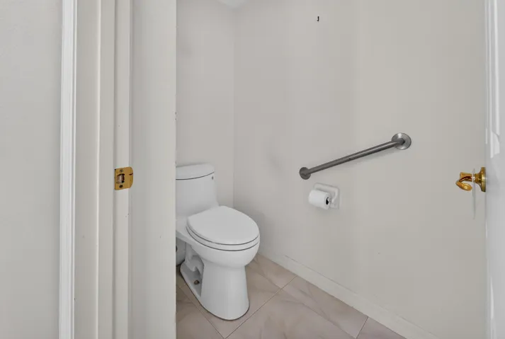 White toilet with dual flush, brushed nickel grab bar, and light-toned tile flooring