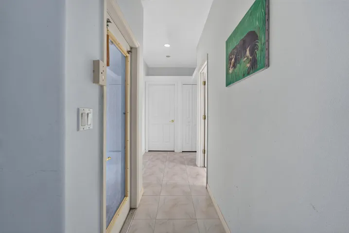 Recessed lighting illuminates the hallway with tile flooring, leading to multiple paneled doors