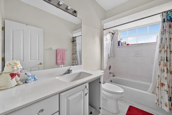 Full bathroom featuring a single vanity with an integrated sink, white cabinetry, a bathtub with a shower, and a large window