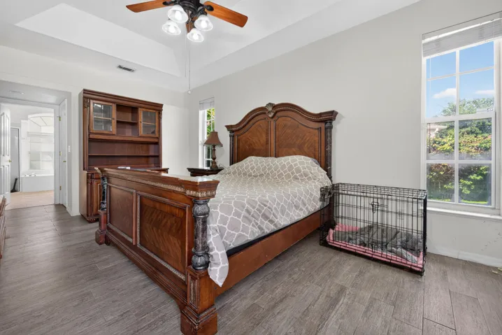 Spacious primary bedroom featuring a wood-finish plank floor, ceiling fan with integrated lighting, and abundant natural light from large windows