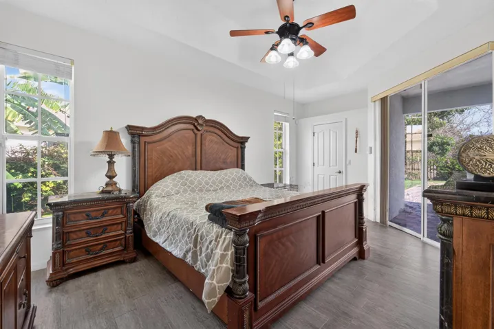 Tray ceiling with a ceiling fan, wood-finish flooring, white walls, large window, and sliding glass door