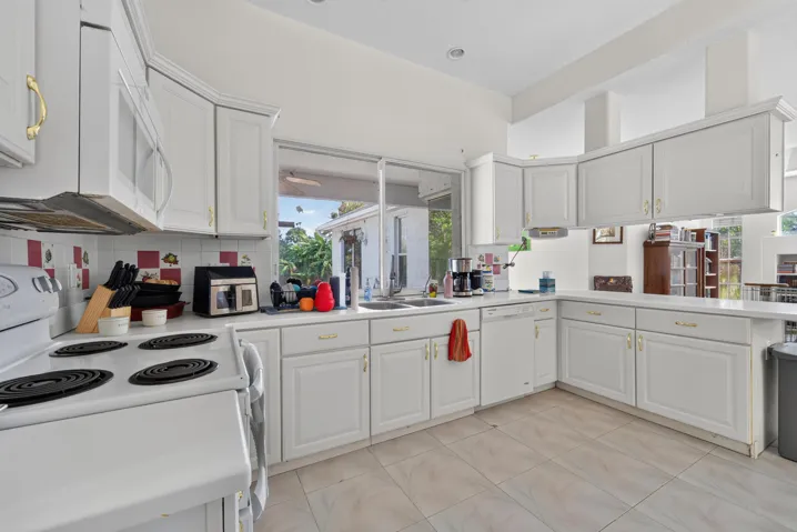 White cabinetry with gold-tone hardware, white countertops, tile flooring, and a kitchen sink with a window above