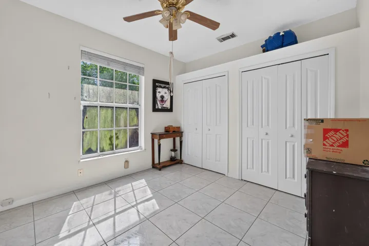 Tile flooring, multiple bi-fold closets, ceiling fan with integrated lighting, and a large window