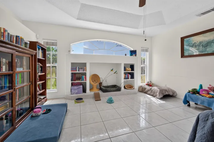 Tray ceiling with a ceiling fan, arched transom window, tile flooring, and built-in shelving units