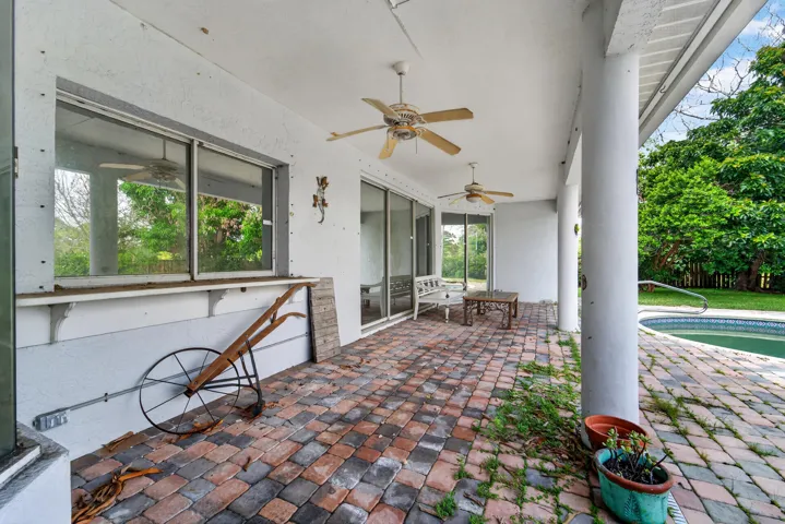 Covered patio with brick paver flooring, multiple ceiling fans, and direct access to an in-ground swimming pool
