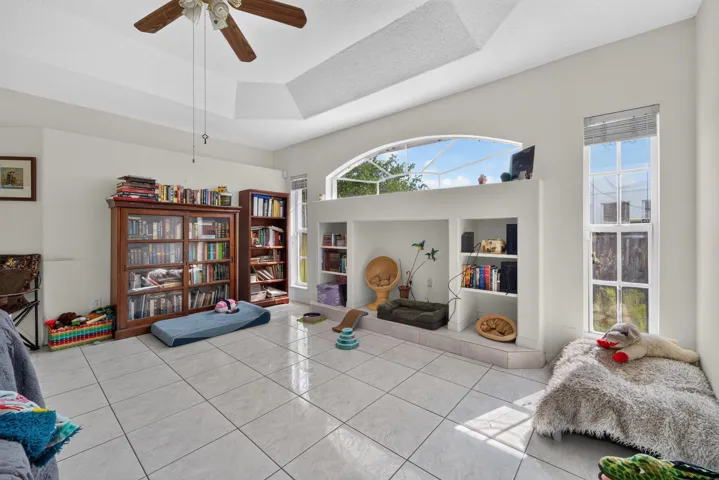 Bright, open recreation room with soaring ceilings, ceiling fan, and abundant natural light from transom and glass doors