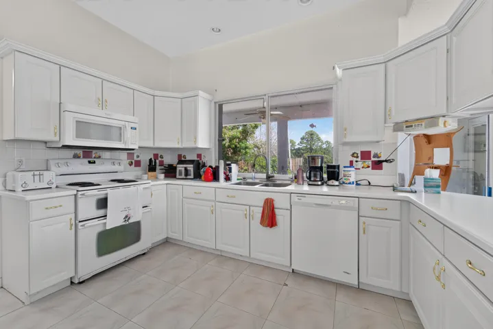 Kitchen with white cabinetry, white appliances, solid surface countertops, and tiled flooring