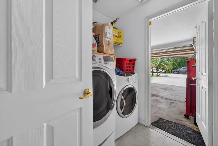 Dedicated laundry room featuring side-by-side front-load washers and dryers, upper cabinetry for storage, tile flooring, and direct access to the exterior