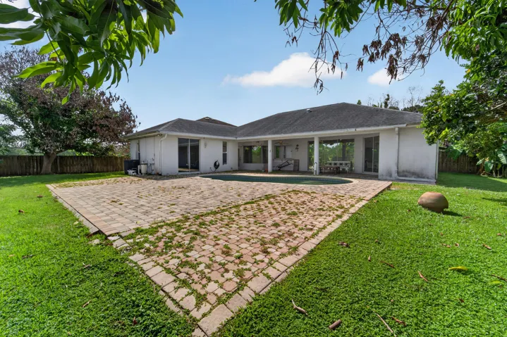 Spacious backyard featuring a large paver patio, lush green lawn, and an in-ground swimming pool