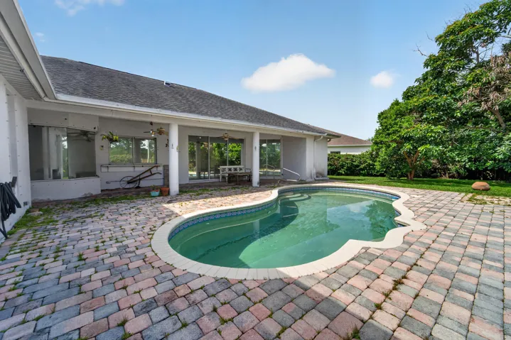 Freeform swimming pool surrounded by a paver patio and mature landscaping