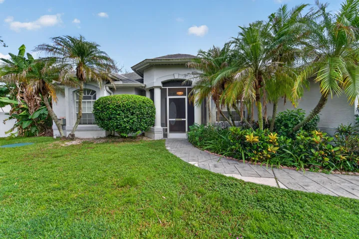 Screened entry, arched window, curved concrete pathway, established palm trees, and mature landscaping