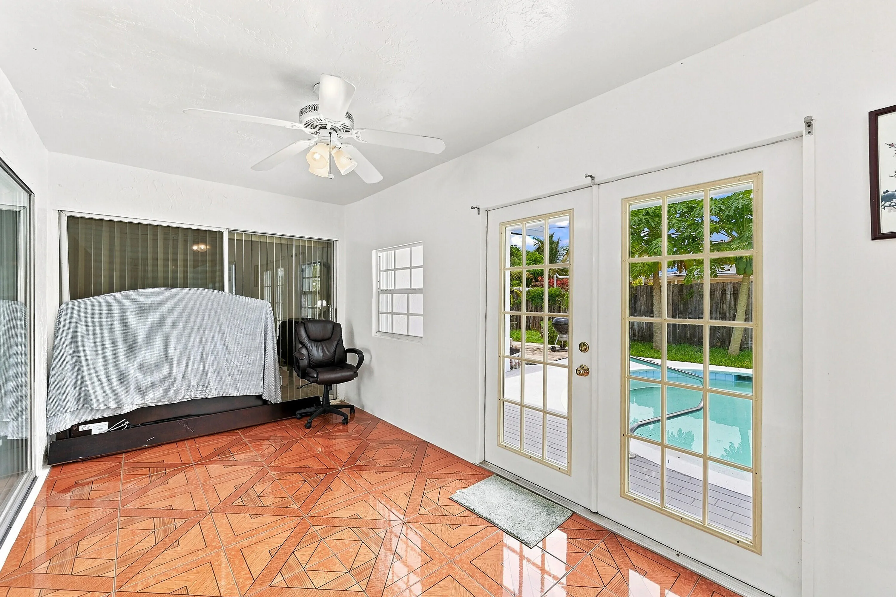Bright Sun Room featuring French doors opening to pool area, wood-finish flooring with geometric pattern detailing, ceiling fan with integrated lighting, and abundant natural light,
