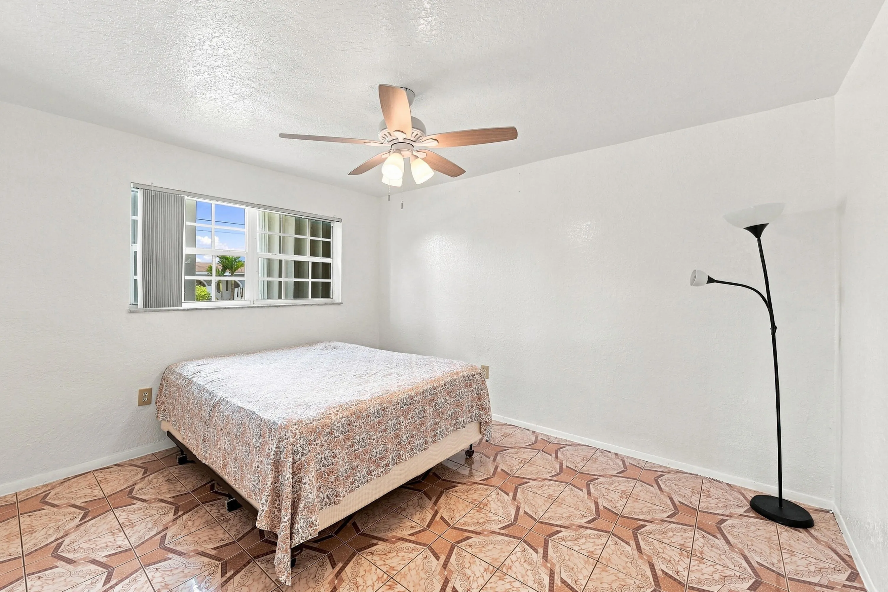 Spacious room featuring patterned tile flooring, a horizontal window with blinds, and a ceiling fan with integrated lighting