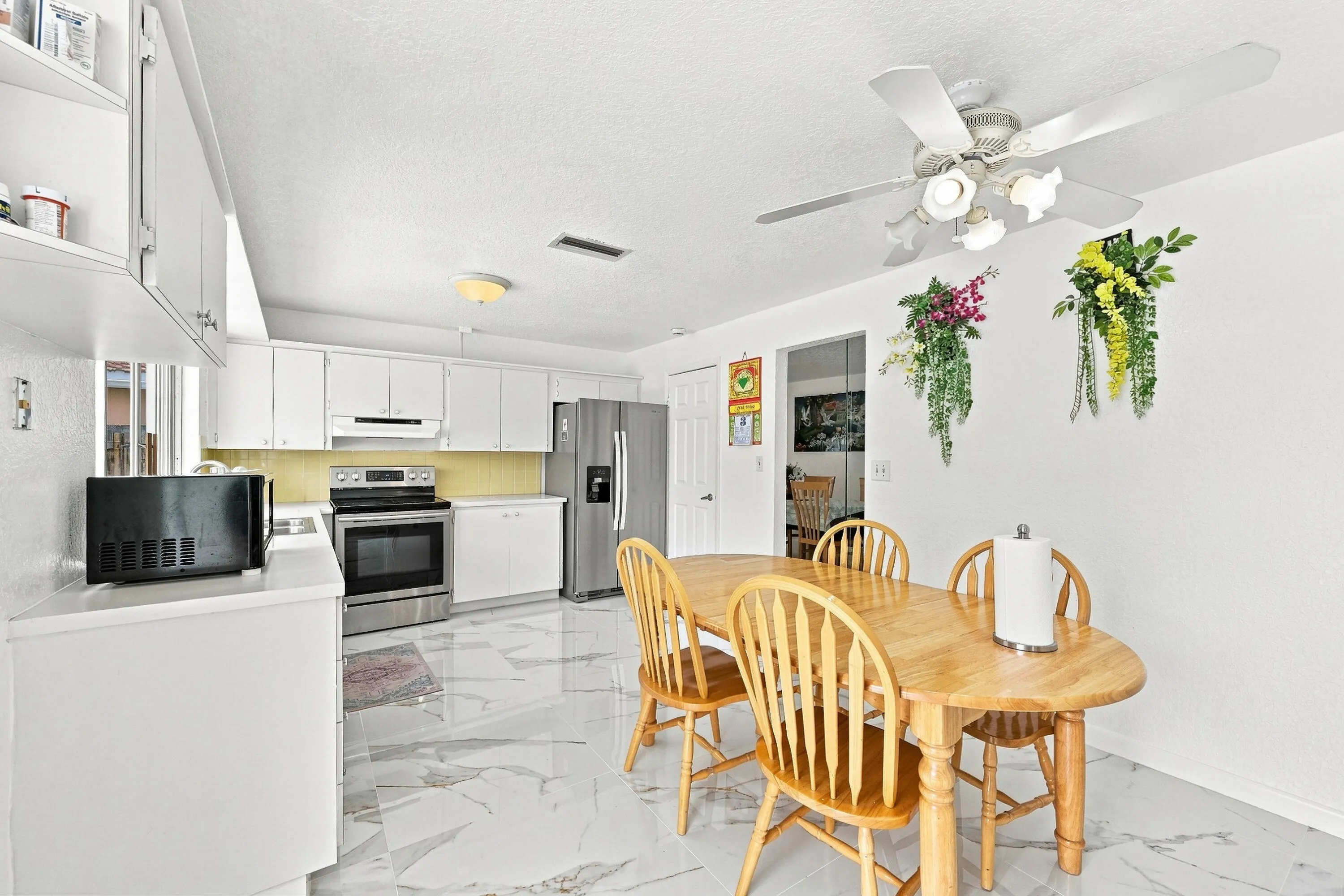 White cabinetry and countertops define this kitchen space, complemented by a yellow backsplash and stainless steel appliances