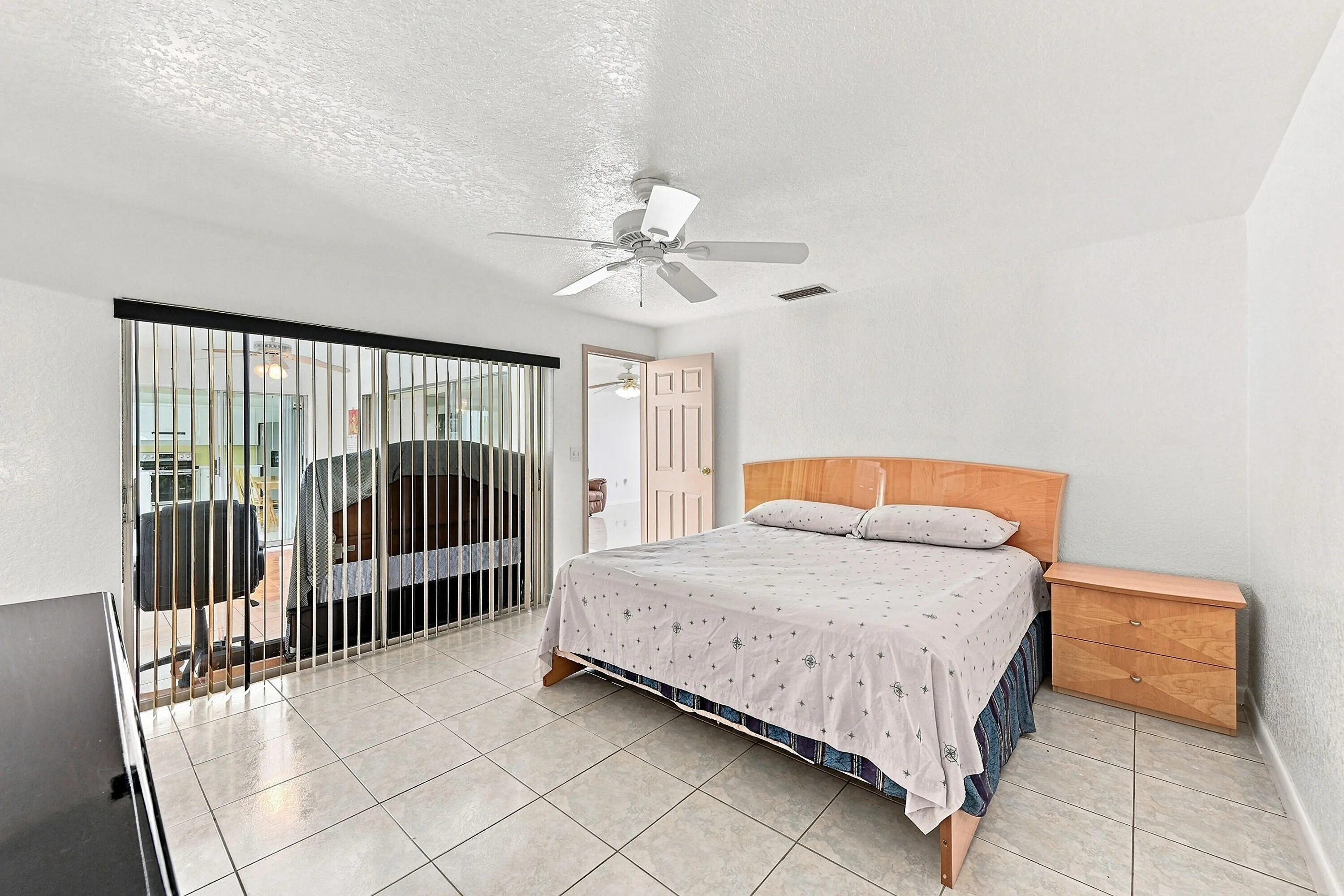 Spacious room featuring tile flooring, a ceiling fan, and sliding glass doors with vertical blinds