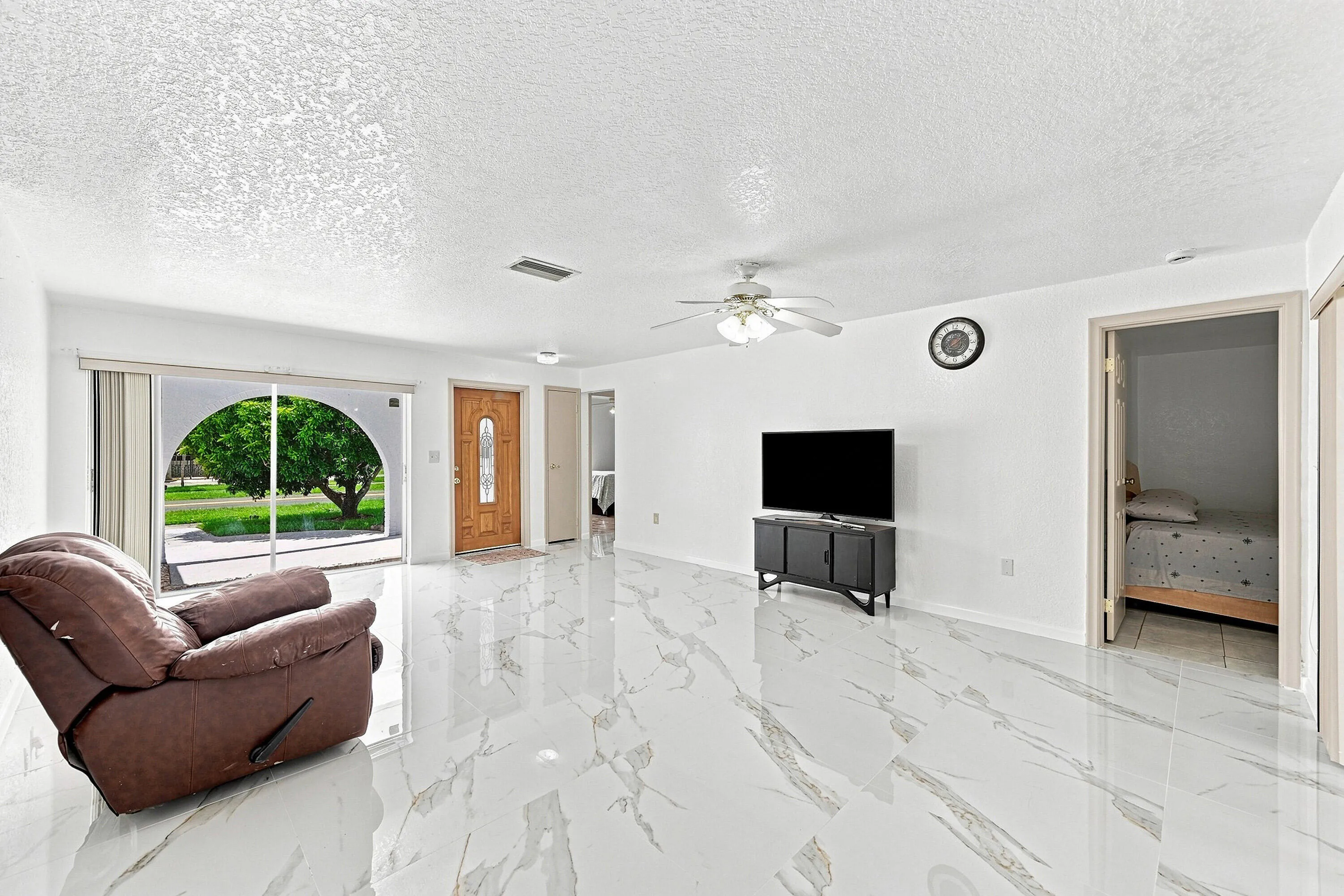 Spacious living area featuring polished tile flooring, a ceiling fan with integrated lighting, and a wood-paneled entry door with decorative glass