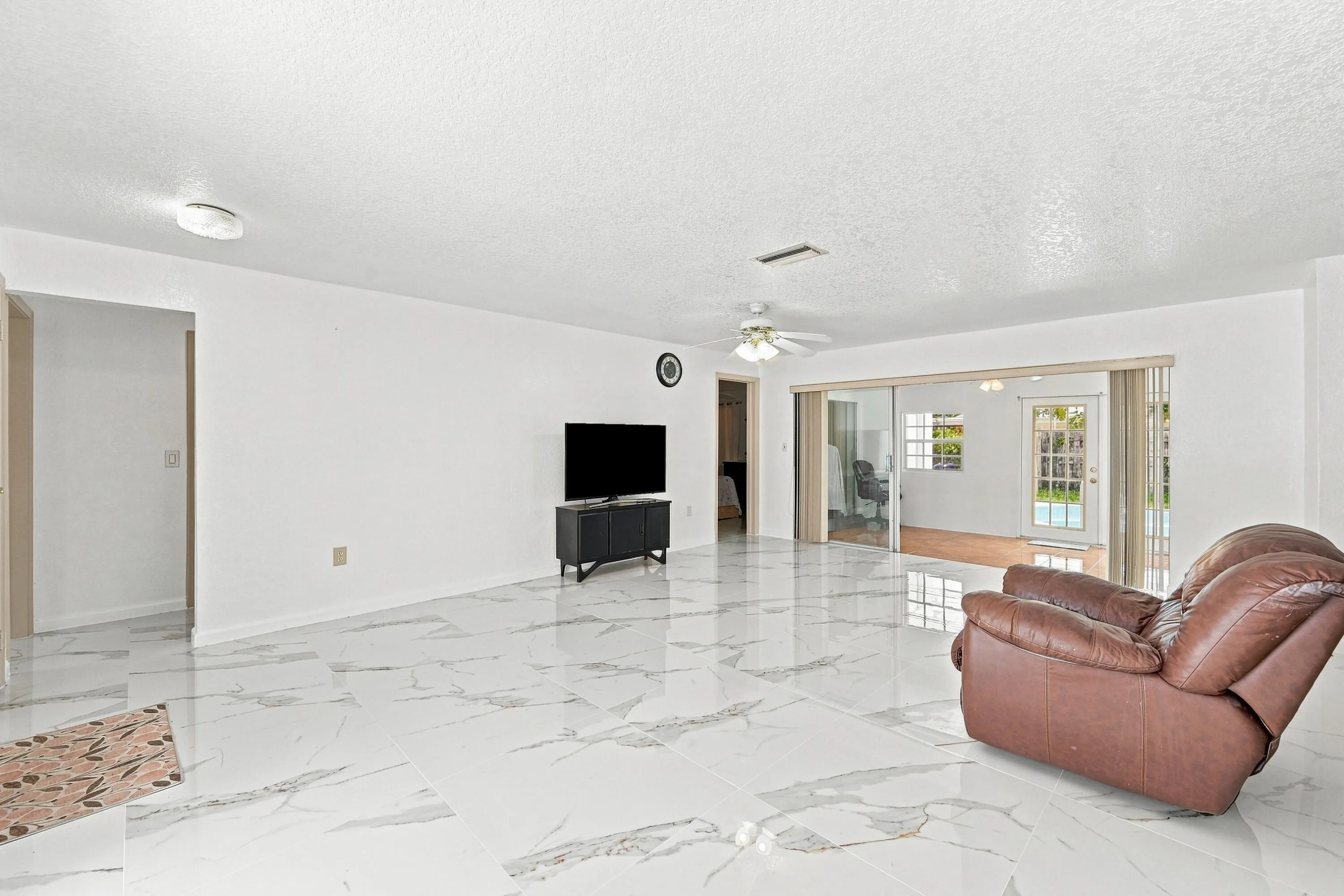 Spacious open-concept living area featuring polished marble-finish flooring throughout, recessed ceiling lighting, and glass sliding doors with transom windows providing natural illumination