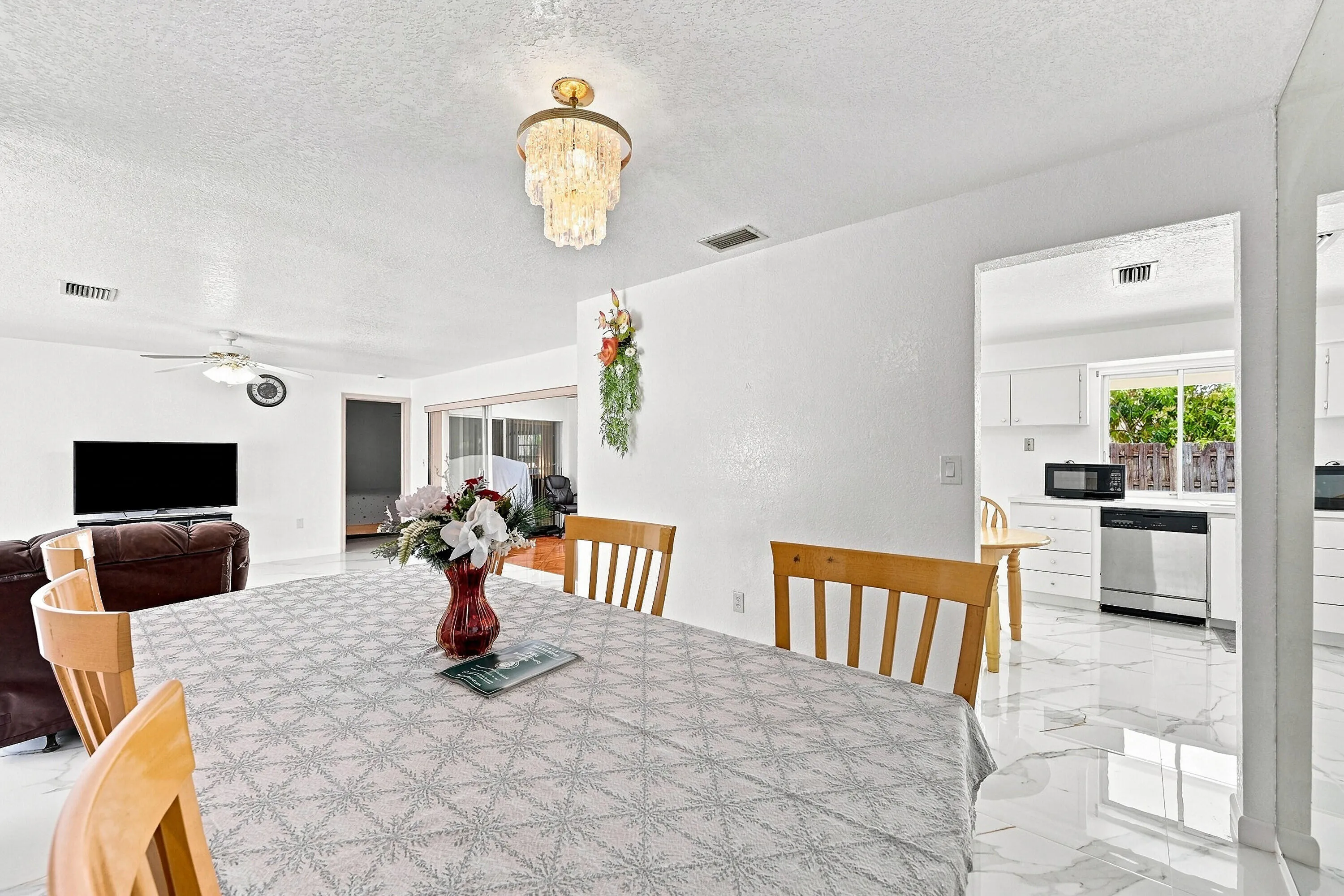 Bright and open dining and kitchen area featuring geometric patterned tile flooring, white cabinetry with stainless steel appliances, recessed lighting, and a brass pendant fixture