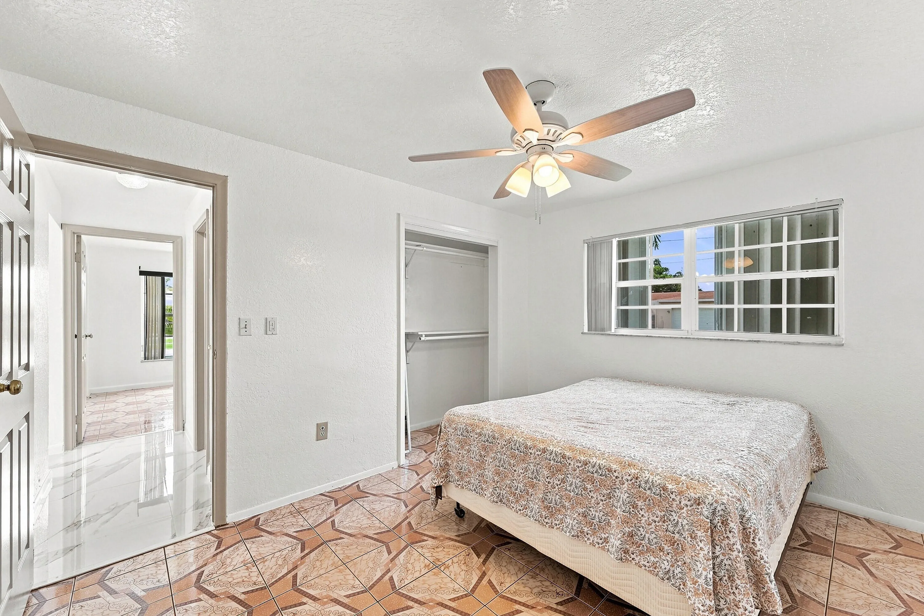 Bright secondary bedroom featuring a ceiling fan with integrated lighting, large multi-pane window with natural light, geometric patterned area rug, and direct access to an ensuite bathroom