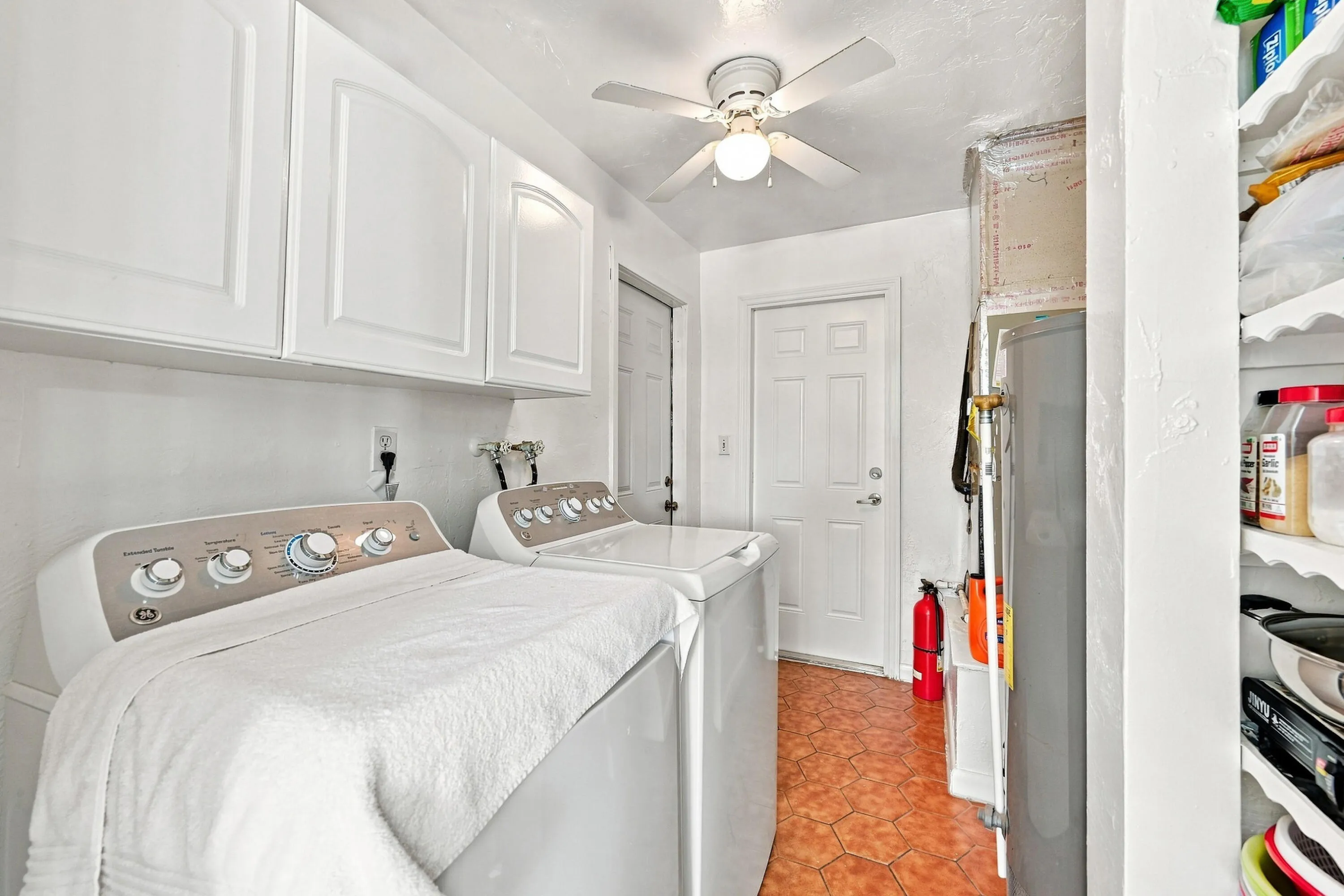 Utility room featuring upper white cabinetry, a ceiling fan with integrated lighting, and terracotta-style hexagonal floor tiles