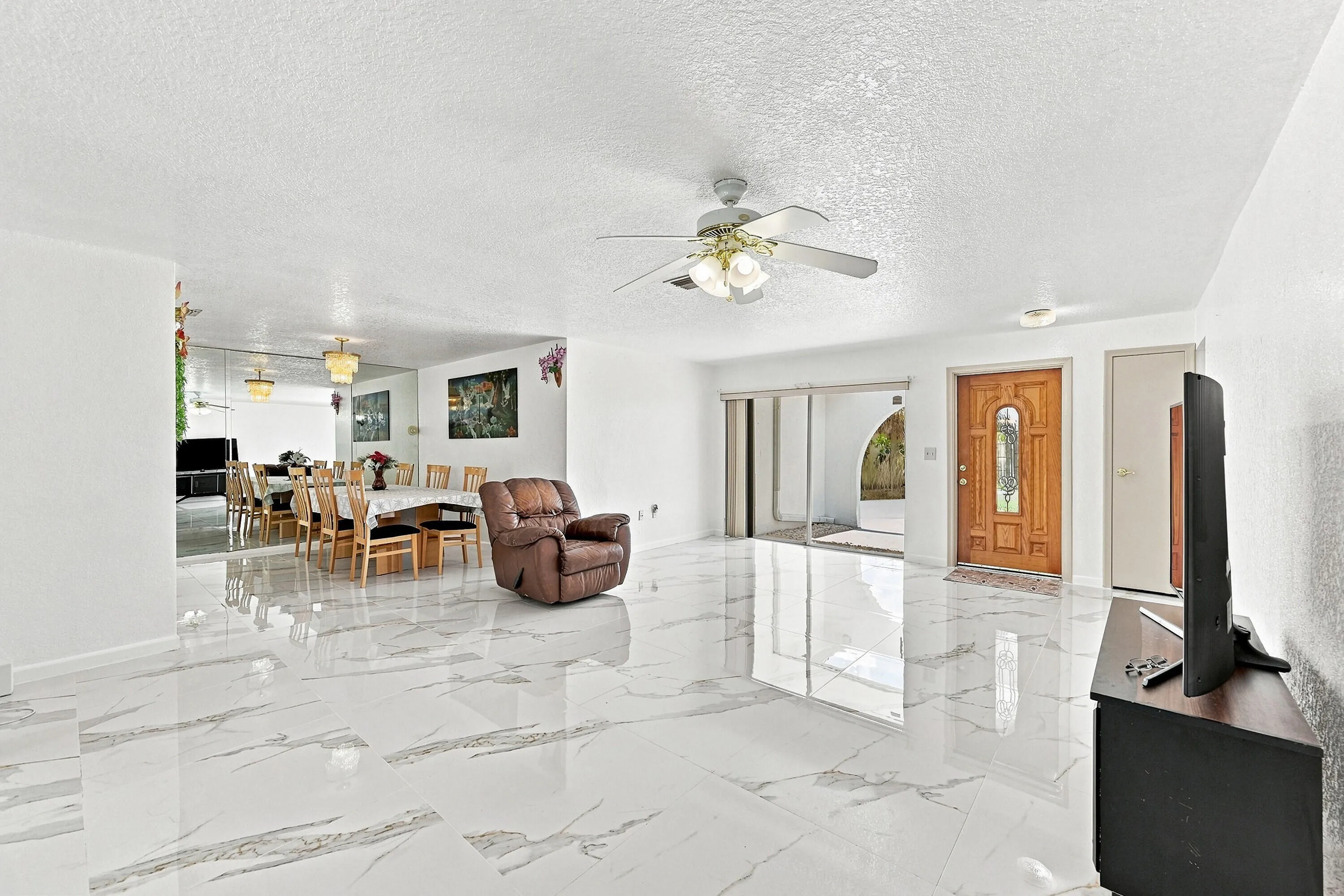 Expansive open-concept living area showcasing polished porcelain tile flooring throughout, recessed ceiling lighting, and a ceiling fan