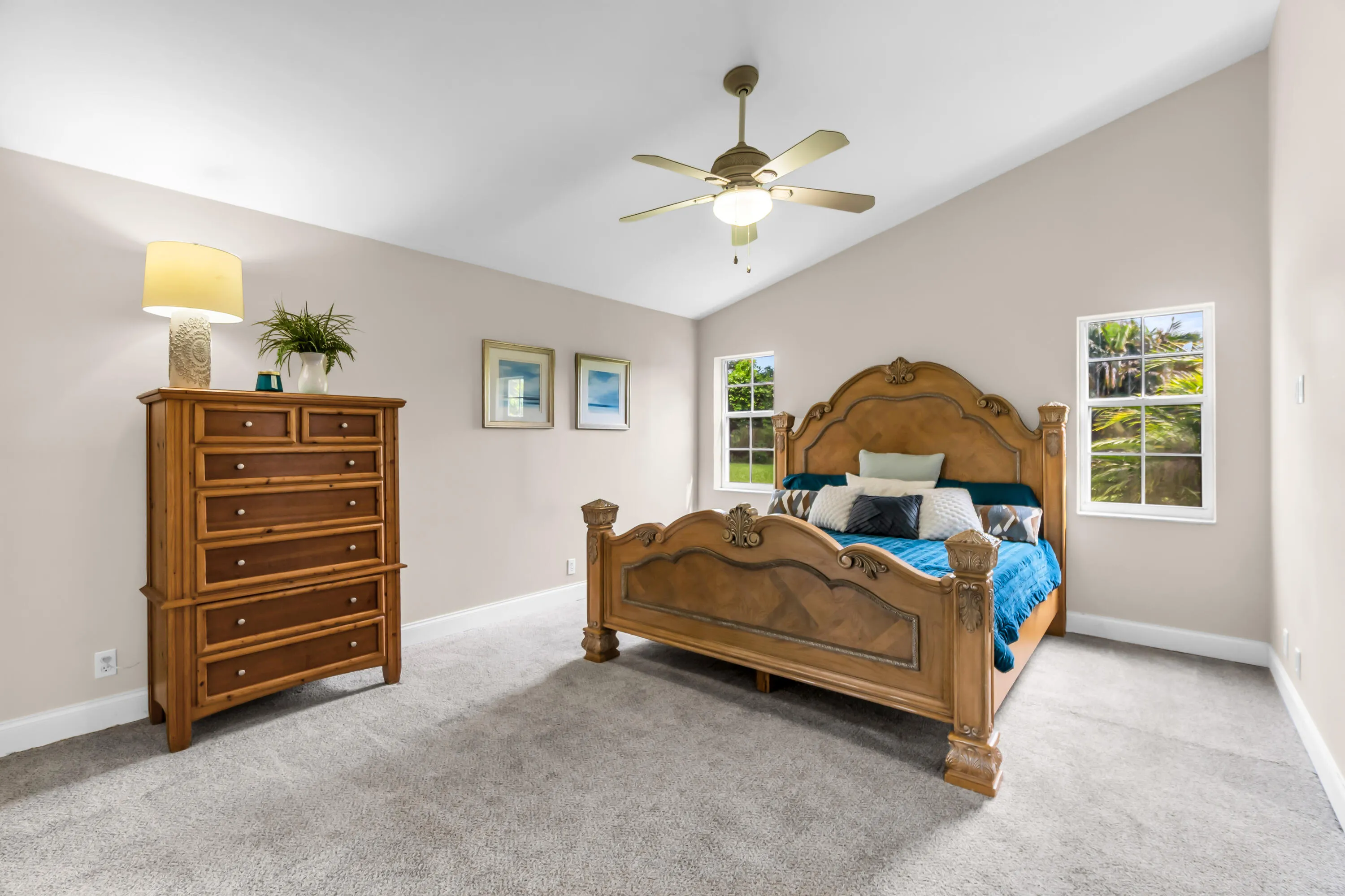Vaulted ceilings enhance this space, featuring neutral wall tones, gray carpeting, dual windows, and a ceiling fan with integrated lighting