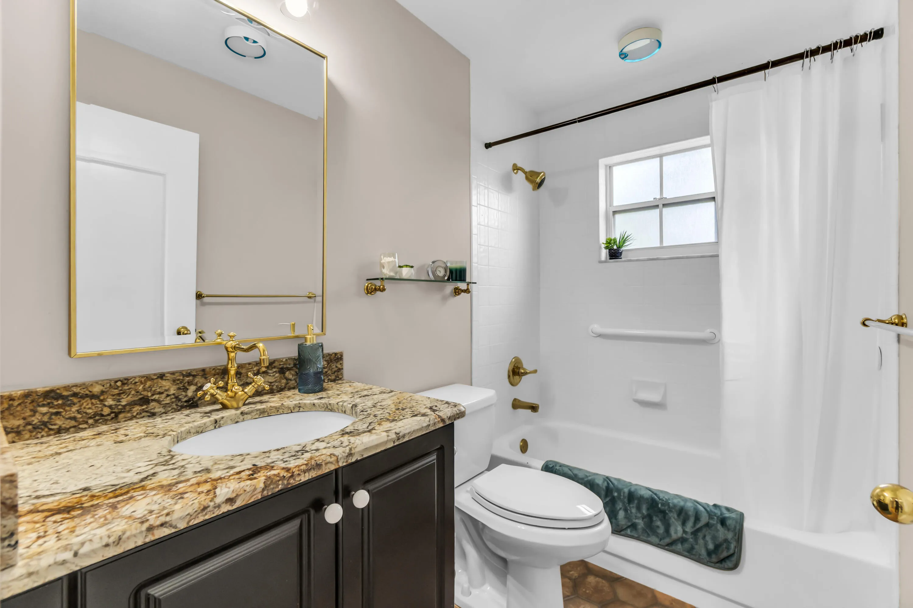 Bathroom featuring a dark wood vanity with a granite countertop, undermount sink, and brass-finish faucet