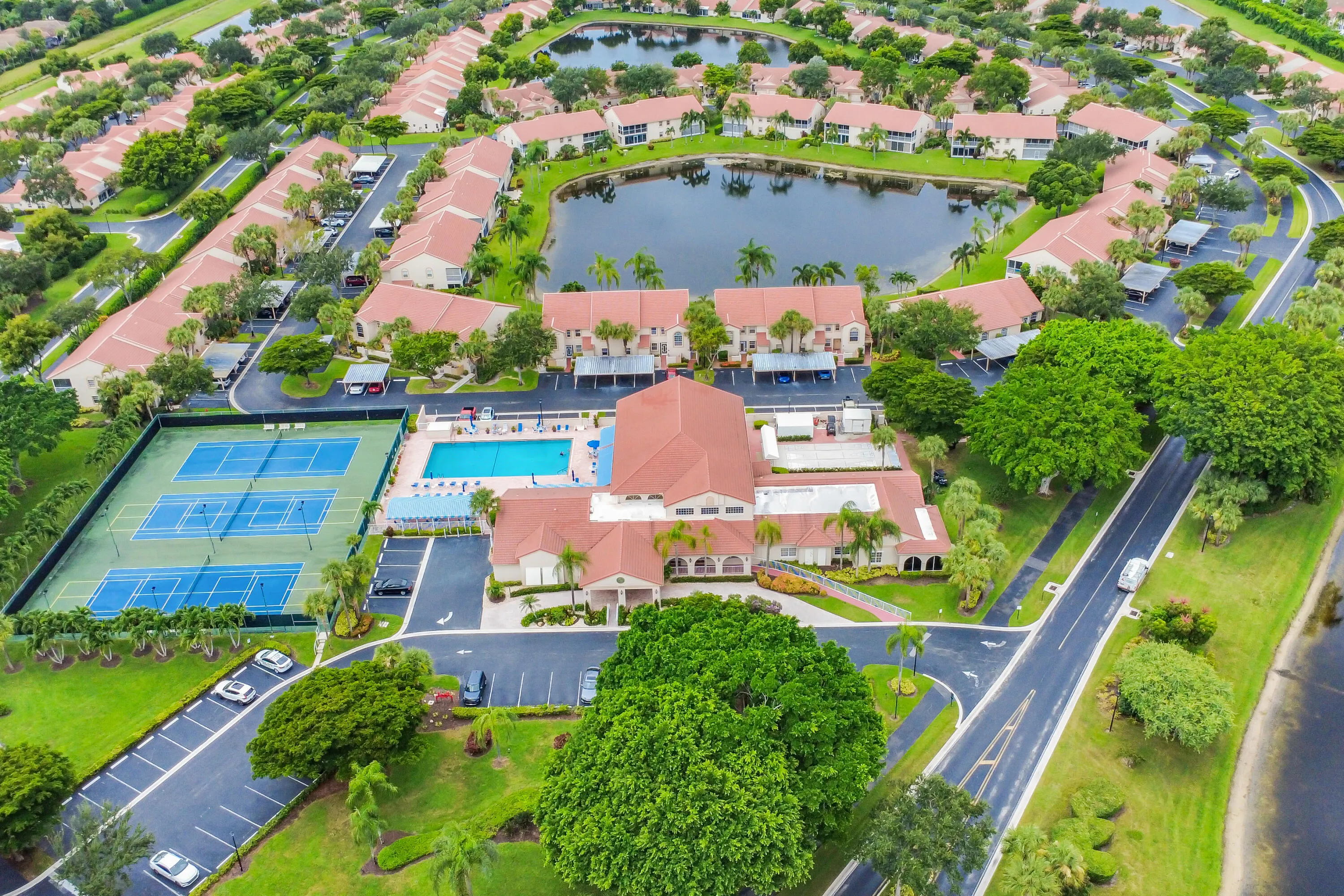 Aerial perspective highlighting a community with a central clubhouse building, outdoor swimming pool, and multiple tennis courts