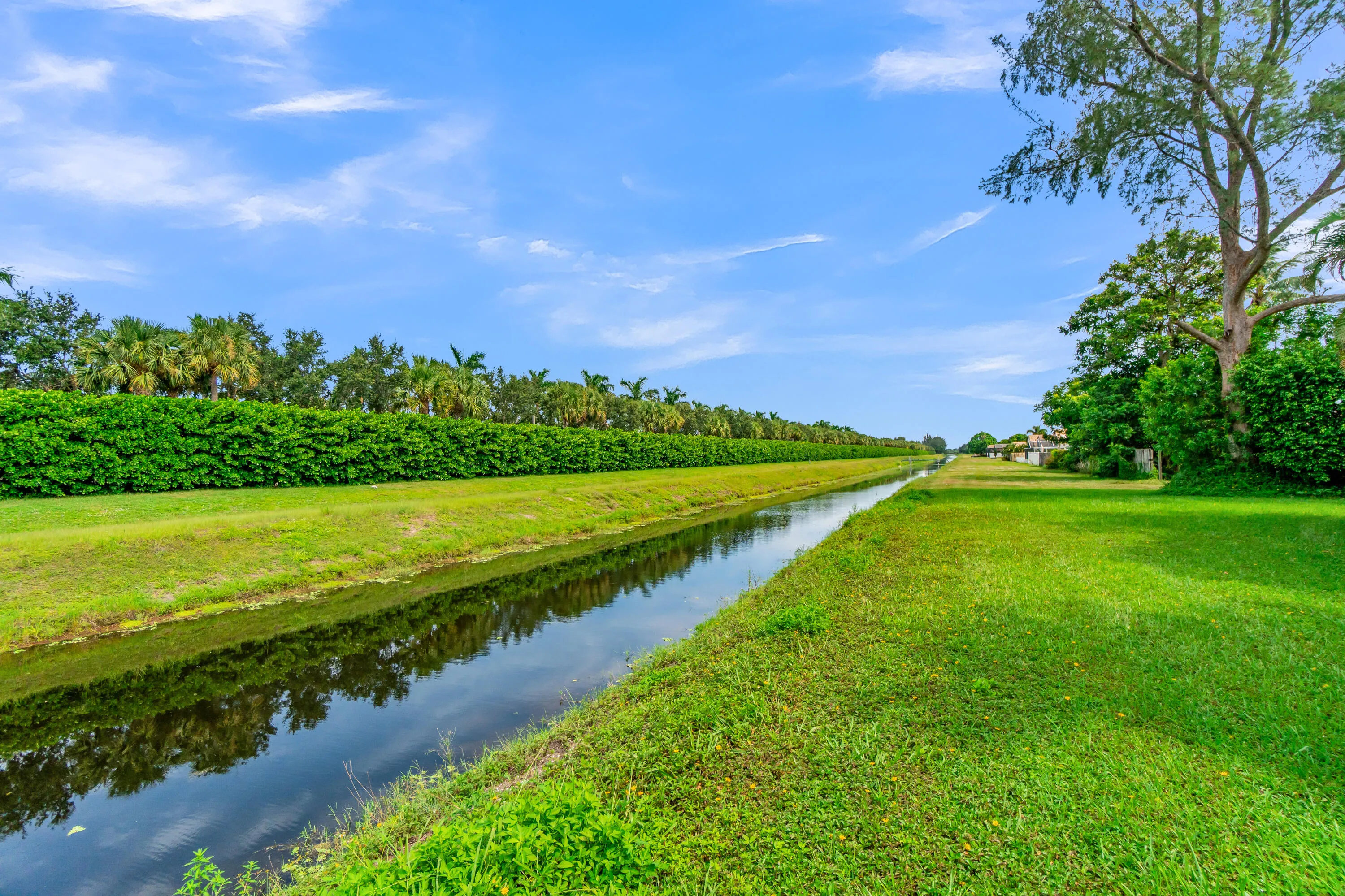 Waterfront property featuring a canal, expansive green space, mature trees, and lush landscaping