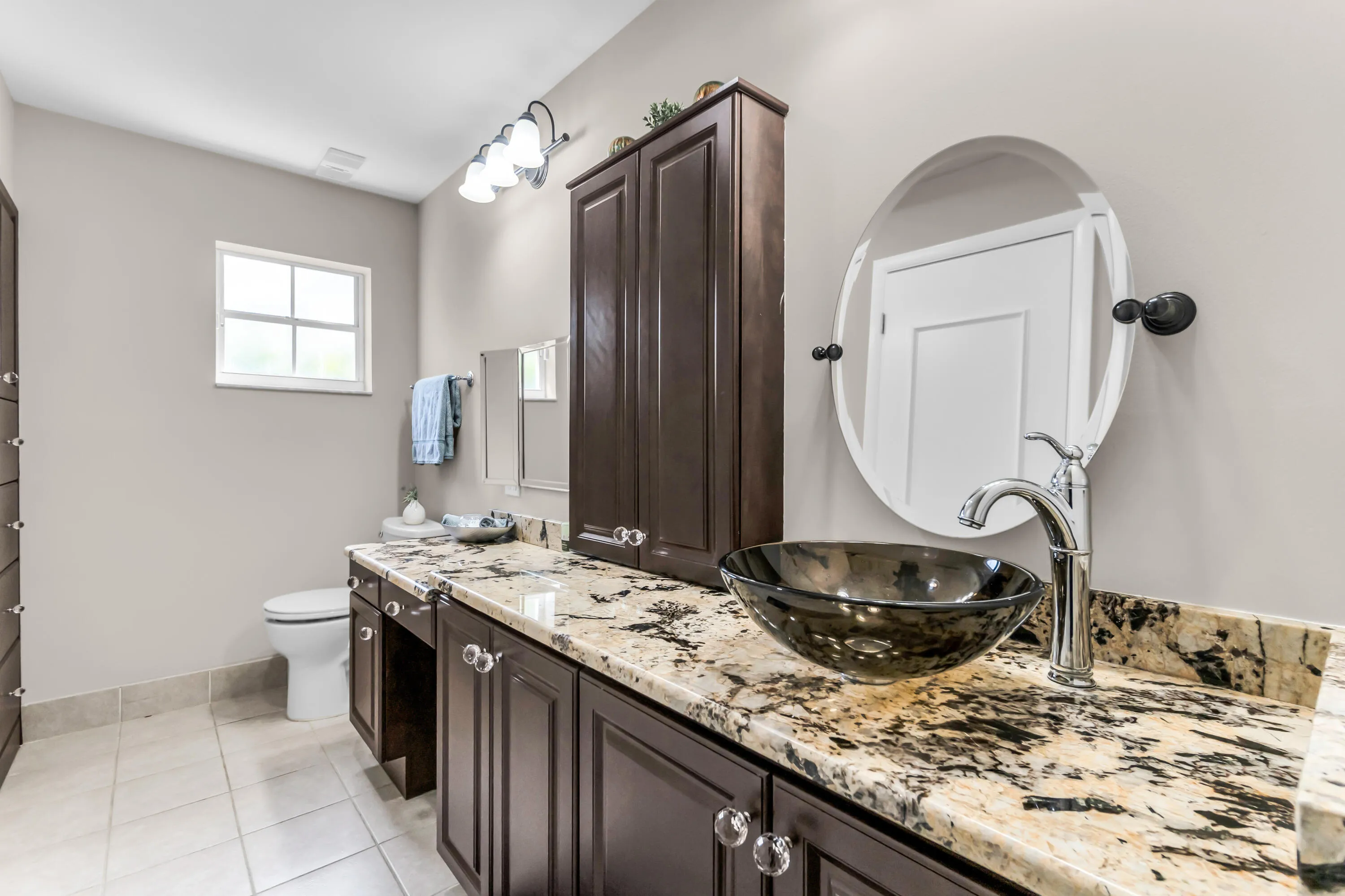 Spacious vanity featuring a vessel sink, variegated countertop, dark wood-finish cabinetry, and an oval mirror