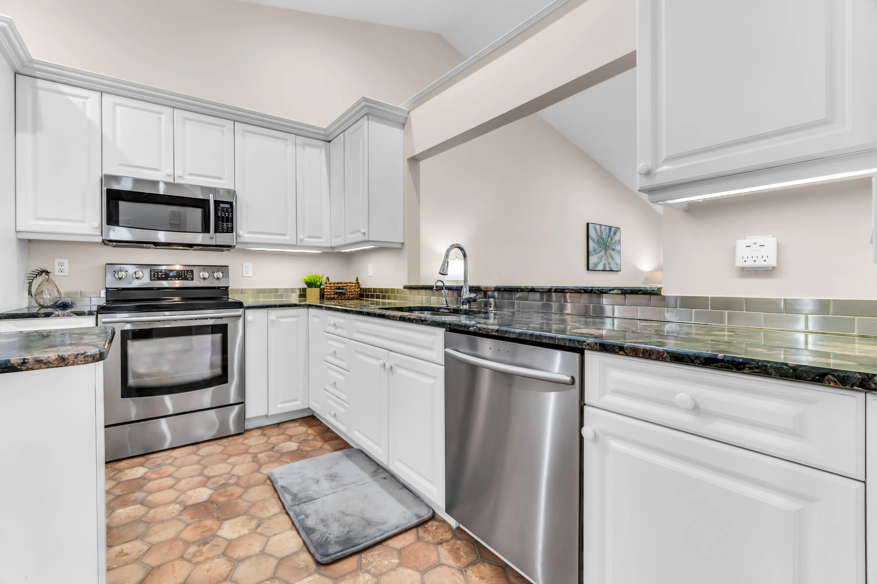 Kitchen featuring white cabinetry, stainless steel appliances, dark stone countertops, a reflective tile backsplash, and hexagonal floor tiling
