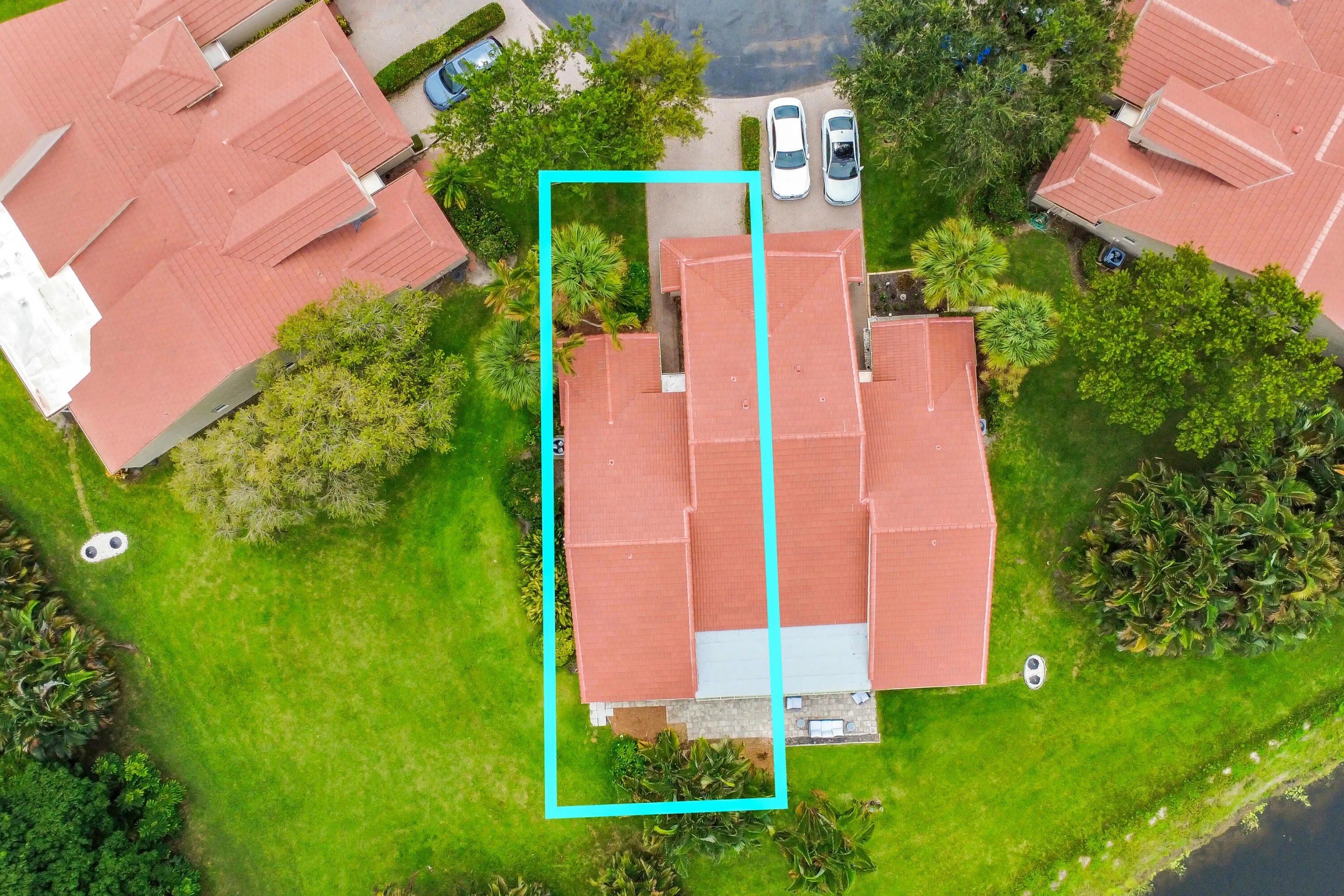 Aerial view of a residential property featuring a terra cotta tile roof, a stone patio, and surrounding green landscaping