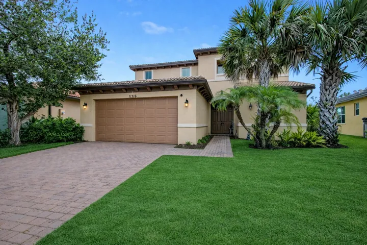 Stucco exterior, barrel tile roof, paver driveway, mature landscaping, and an integrated garage