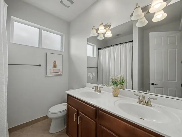 Master bathroom featuring a dual-sink vanity with wood-finish cabinetry and white quartz countertops, chrome faucet fixtures, and an undermount basin design