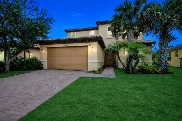 Two-story stucco exterior with a tile roof, paver driveway, and mature landscaping