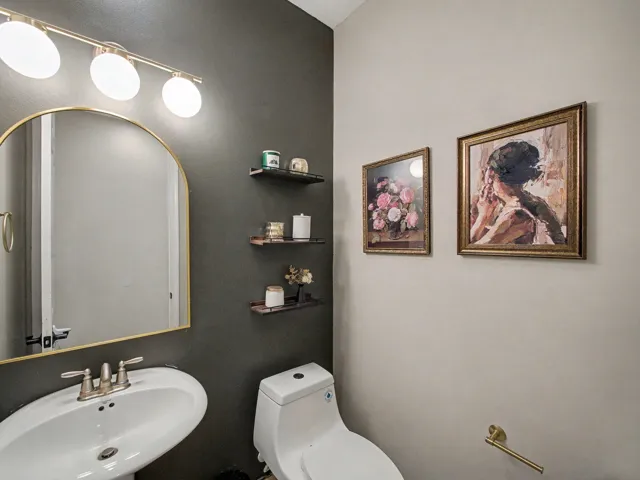 Pedestal sink with brushed nickel faucet, arched mirror with gold-tone frame, and overhead vanity lighting