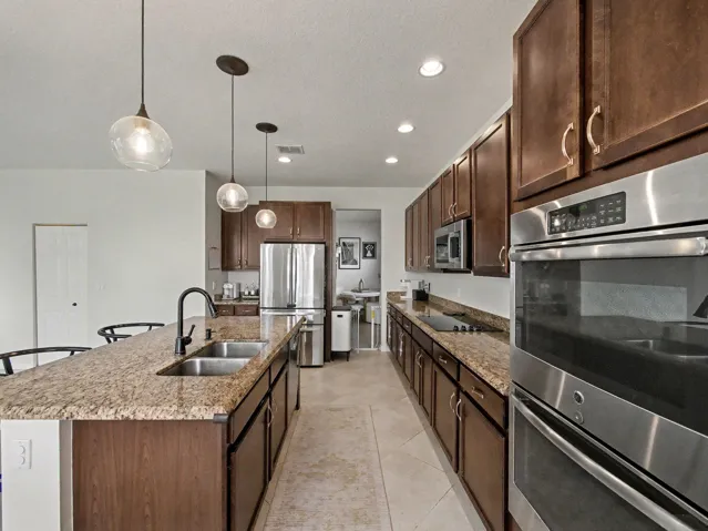 Expansive kitchen featuring a large island with dual sinks, built-in stainless steel appliances, abundant cabinetry, and granite countertops