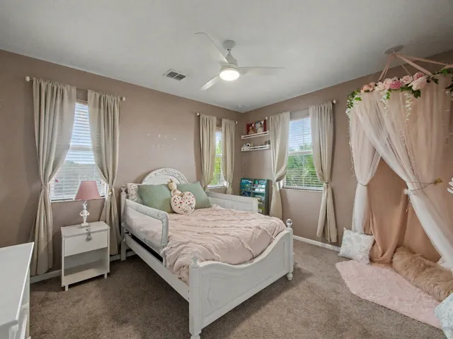 Plush carpeted flooring, multiple windows with blinds, a ceiling fan with integrated lighting, and a neutral wall color