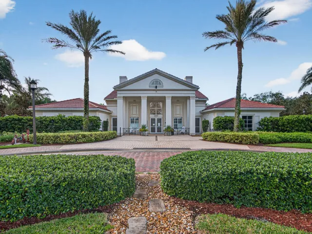 Neoclassical architecture with a columned portico, a red tile roof, and a brick paver driveway