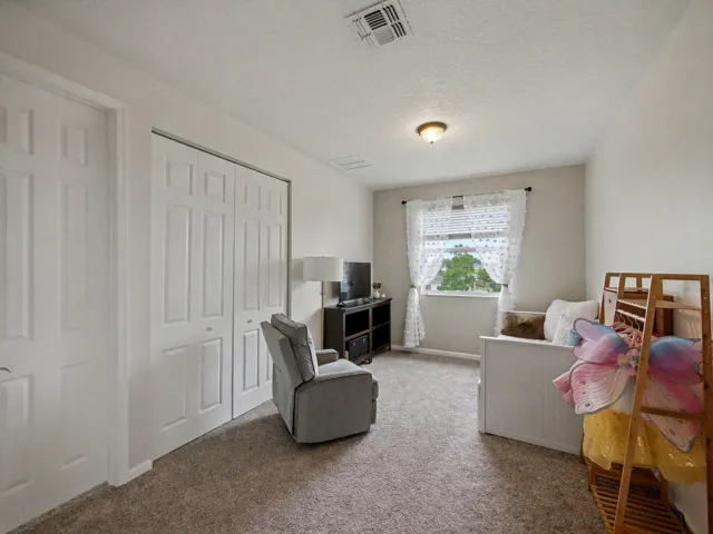 Carpeted flooring, window with natural light, textured ceiling, ceiling-mounted light fixture, and white bi-fold closet doors