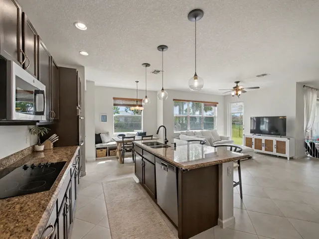 Kitchen featuring an island with a built-in sink, dark cabinetry, and granite countertops