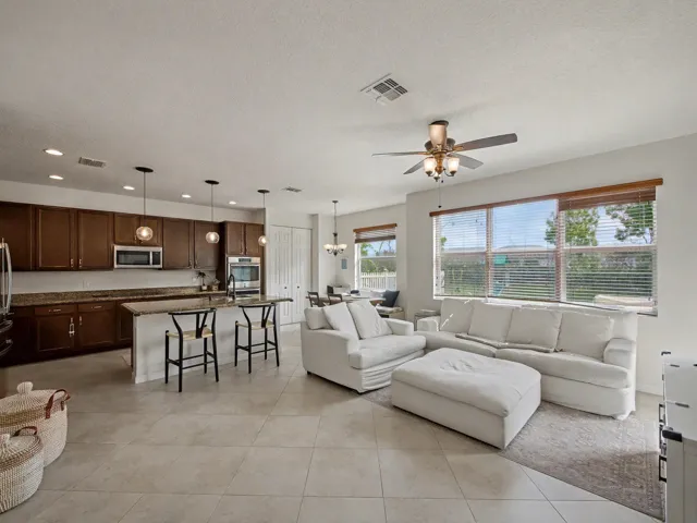 Spacious open-concept living area featuring large format tile flooring, a kitchen island with seating, pendant lighting, recessed lighting, and a ceiling fan