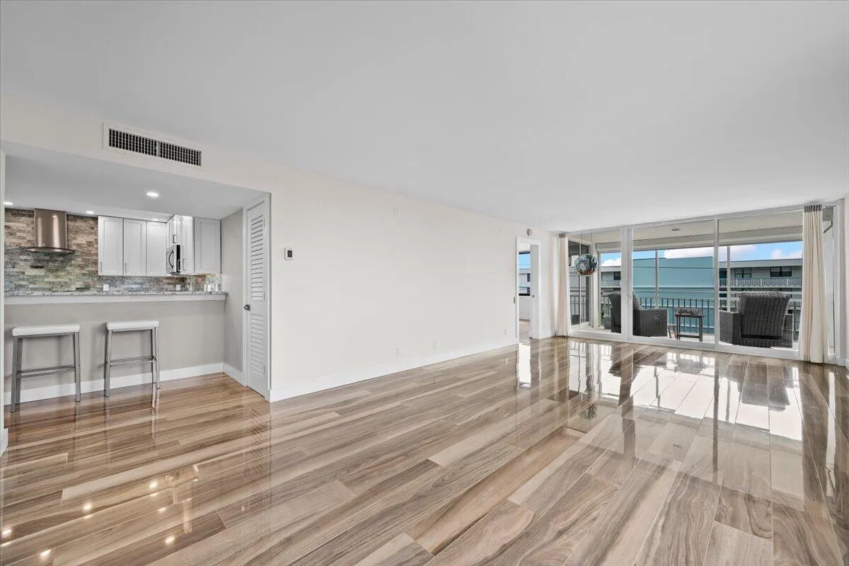 Open-concept living area featuring wood-finish flooring, a kitchen with light cabinetry, and a full-height glass sliding door opening to an outdoor balcony