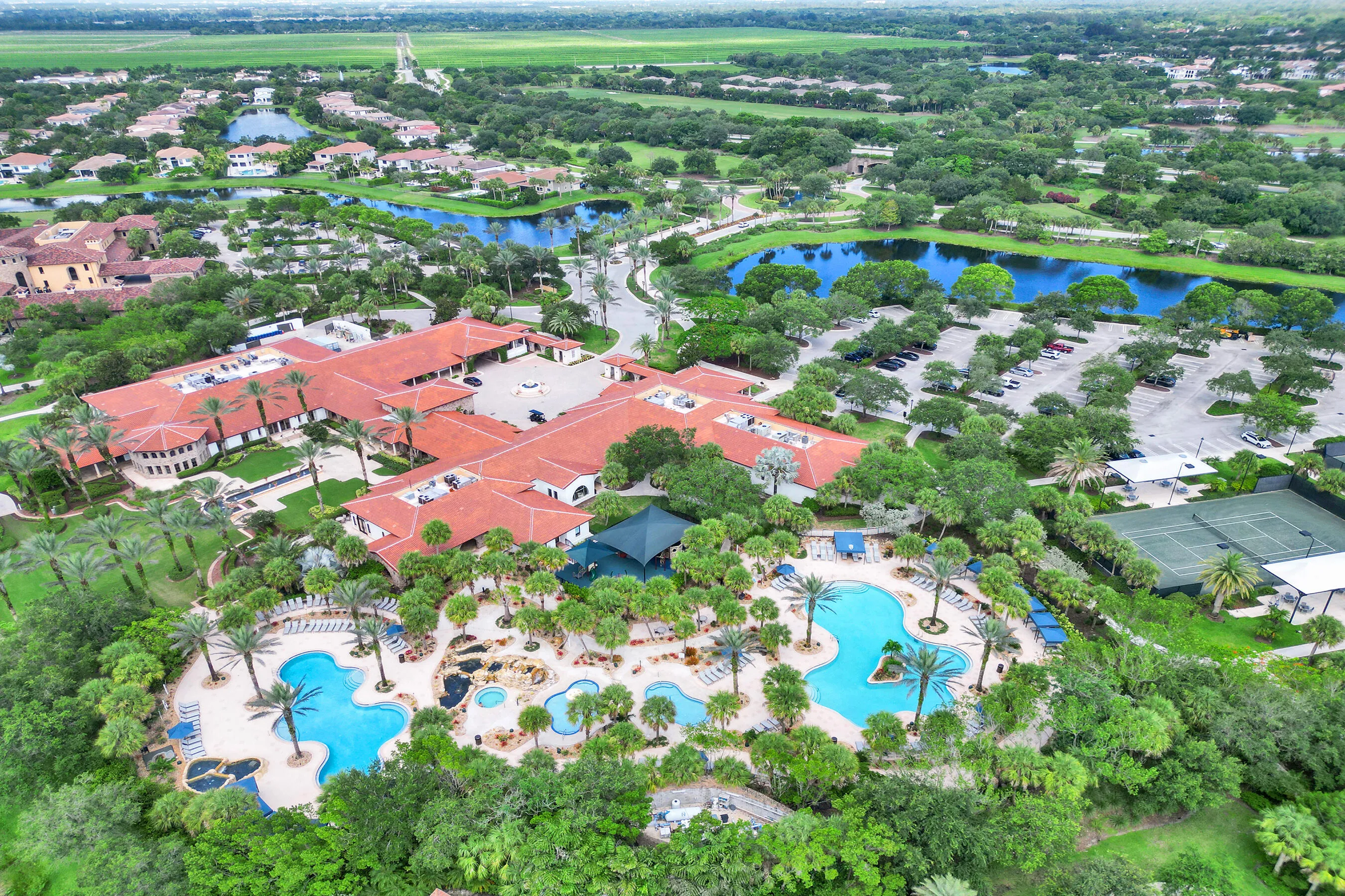 Expansive property featuring multiple aquatic areas, tennis courts, a large building with a tile roof, and abundant mature trees