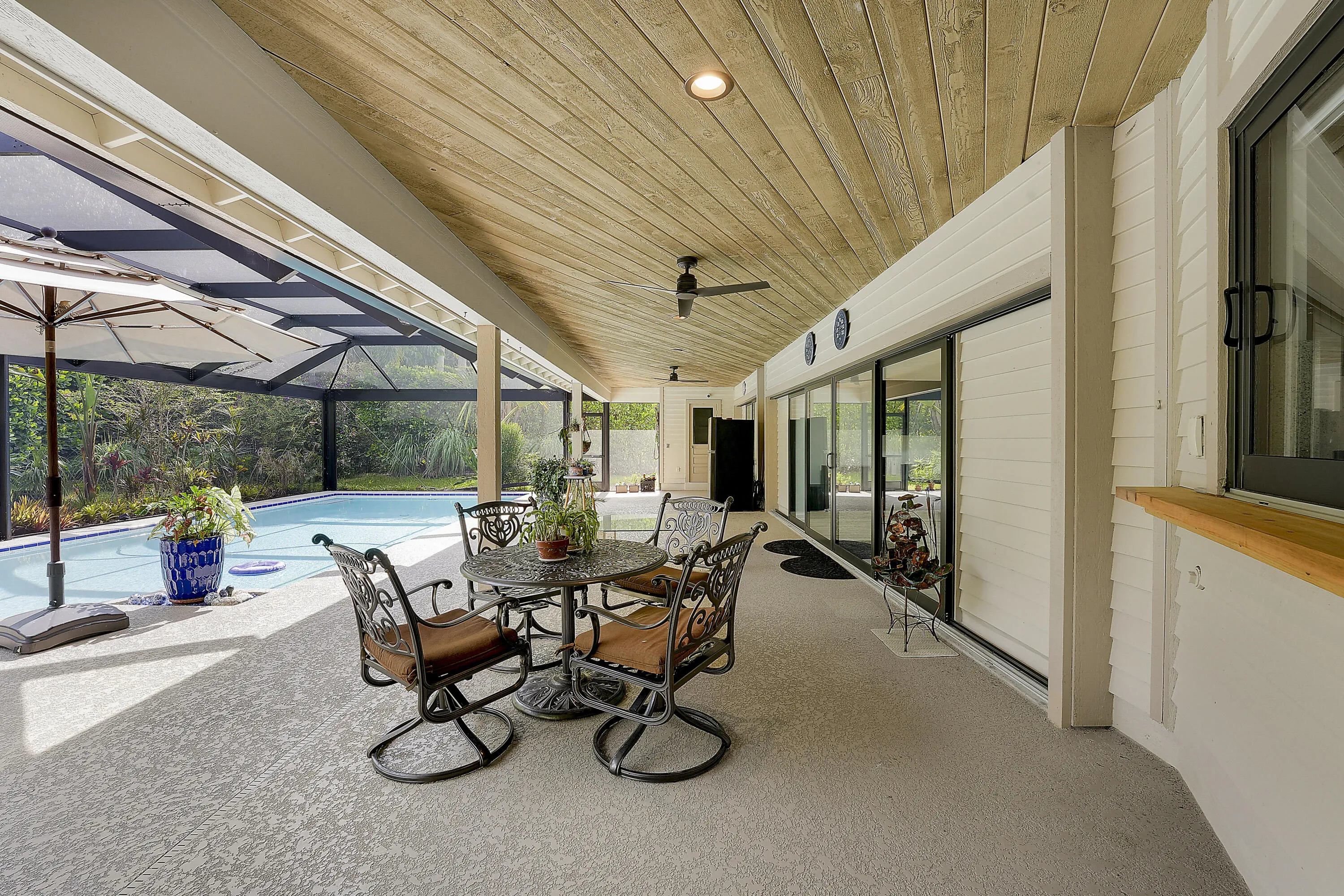 Inviting covered patio with dining area and views of the screened saltwater pool, surrounded by lush tropical landscaping.